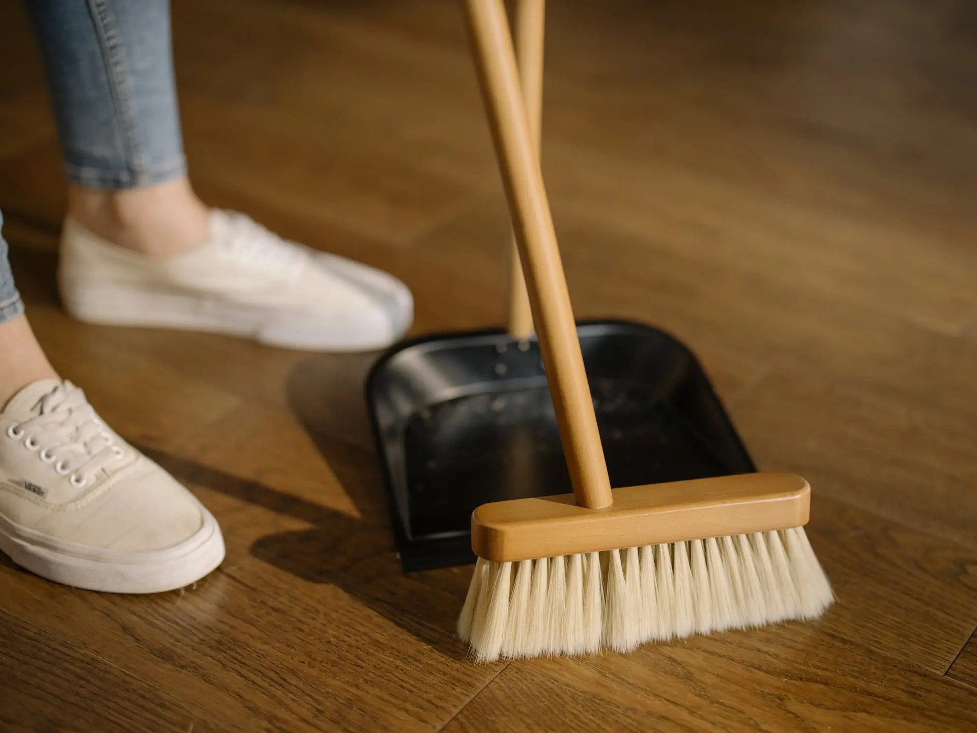 Person using dust and broom on wooden floor